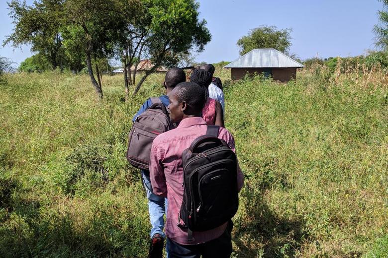 Men walking in a line through grass in Siaya Kenya
