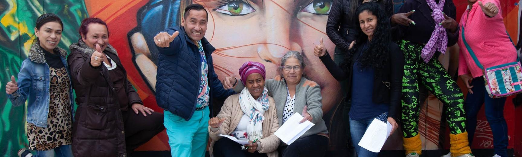People hold their thumbs up to the camera in front of wall art in Bogota, Colombia