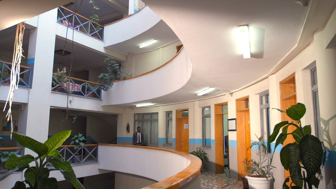 Person walking through hallway with lots of doors in a building with balconies and plants in Ethiopia
