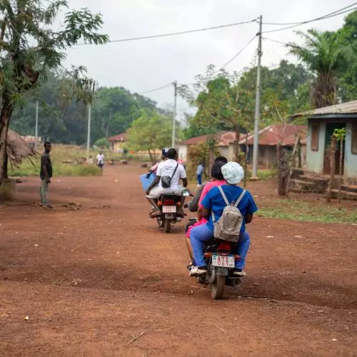 Photo of motorbike drivers and health workers delivering vaccines through a village in rural Sierra Leone