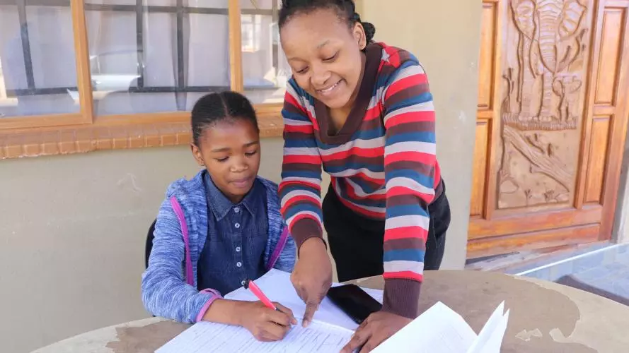 Young girl does work in a workbook with a teacher helping her