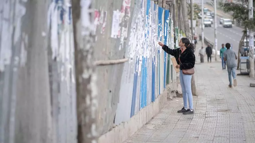 Woman searching through job adverts on a long wall by a road in Ethiopia